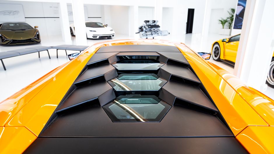 Detailed view of an orange supercar's engine cover in a modern luxury showroom.